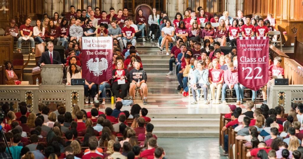College Events At The University Of Chicago. A Large Crowd In A Fancy Hall With People Wearing Brown And Holding Banners