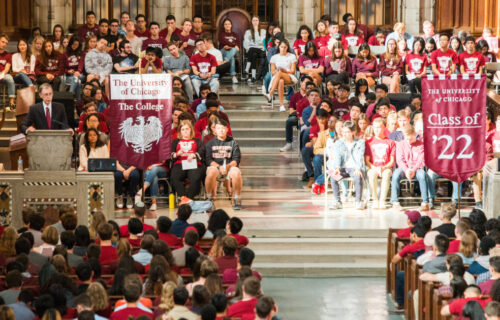 College Events At The University Of Chicago. A Large Crowd In A Fancy Hall With People Wearing Brown And Holding Banners